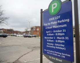 A blue parking sign in front of a parking lot with vehicles.